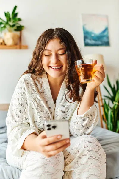 A young plus size woman relaxes at home, sipping a drink and browsing her phone. — Stock Photo