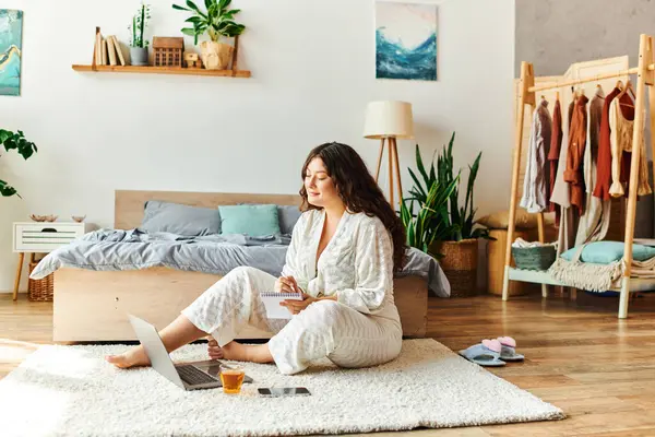 Uma jovem relaxa confortavelmente em sua elegante casa, navegando em um laptop com chá. — Fotografia de Stock