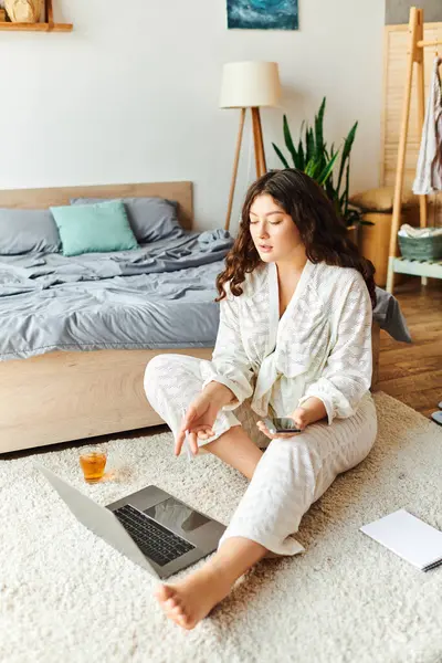 Una joven hermosa mujer de tamaño grande se relaja en casa, comprometida en el trabajo creativo en su computadora portátil. - foto de stock