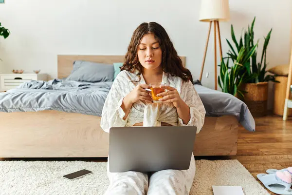 A young woman relaxes at home, sipping a drink and focused on her laptop in a cozy space. — Stock Photo