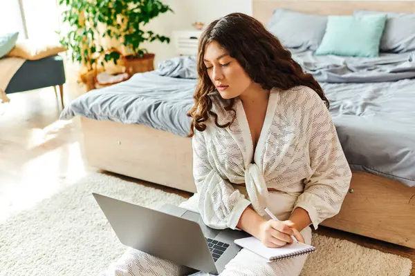 In a serene bedroom, a beautiful plus size woman focuses on her laptop while taking notes. — Stock Photo