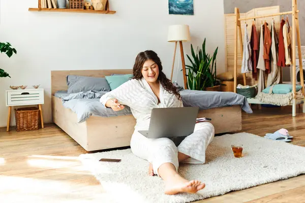 A young beautiful plus size woman relaxes at home, focusing on her laptop with delight. — Stock Photo