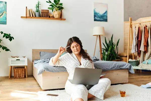 Eine junge Plus-Size-Frau genießt ihren Laptop, während sie sich in einem stilvollen, einladenden Schlafzimmer entspannt. — Stockfoto