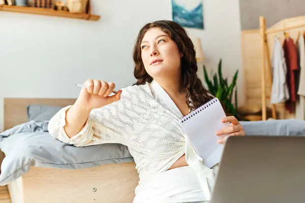 A young plus size woman relaxes at home, jotting down ideas in her notebook with a pensive look. — Stock Photo