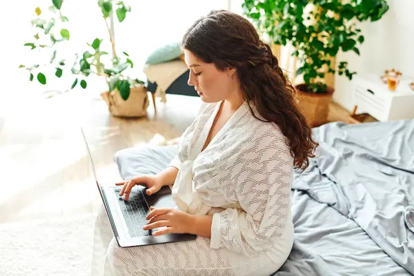 Женщина plus size занимается с ноутбуком, удобно сидя на кровати в окружении зелени. — стоковое фото