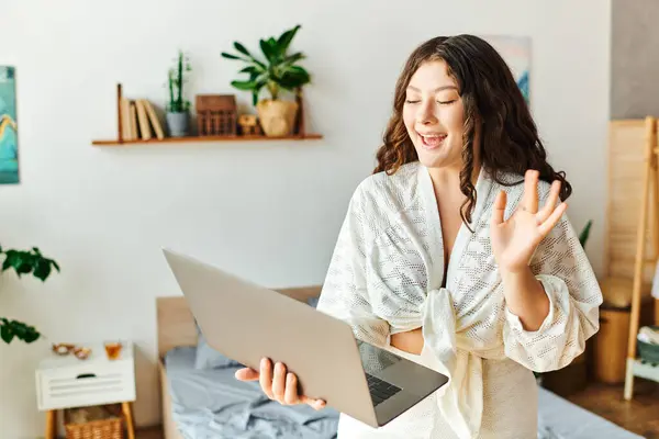 The young woman engages with her laptop, smiling and waving enthusiastically in her cozy room. — Stock Photo