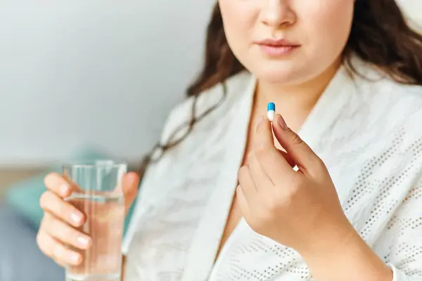 A young beautiful woman at home holds a pill in one hand and a glass of water in the other. — Stock Photo