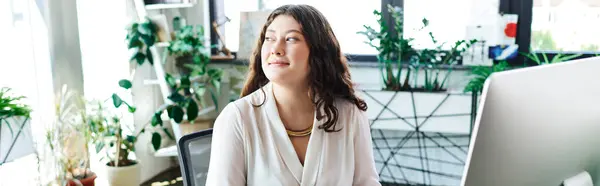 A plus size woman smiles warmly while working at her office, filled with plants. — Stock Photo