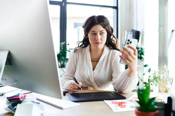 A young plus size woman is focused on her smartphone while engaged in creative work at office. — Stock Photo