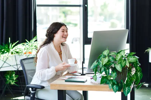 A radiant young woman sips coffee and smiles at her computer in a sunlit office. — Stock Photo