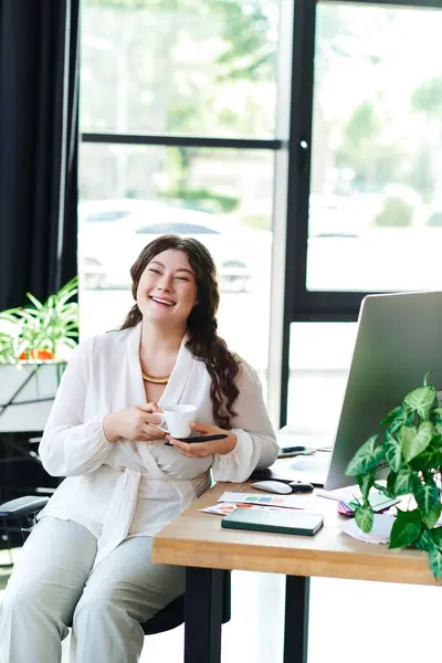 Die junge Plus-Size-Frau genießt einen ruhigen Nachmittag im Büro, nippt an ihrem Tee und lächelt. — Stockfoto