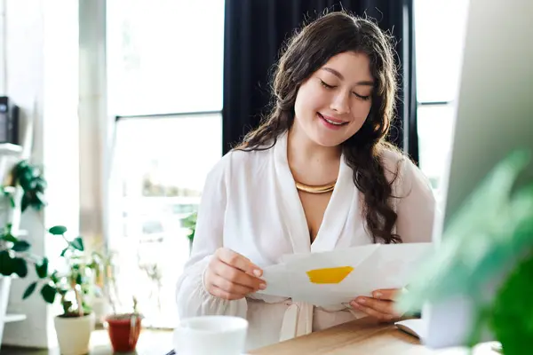Женщина plus size улыбается, рассматривая свои работы в уютном, светлом углу своего офиса. — стоковое фото