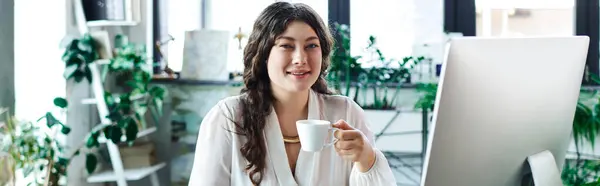 Веселая женщина улыбается, потягивая кофе на рабочем месте в офисе, в окружении растений. — стоковое фото