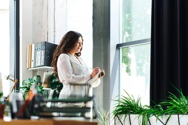 A confident young plus size woman enjoys a creative moment at office, writing and reflecting. — Stock Photo