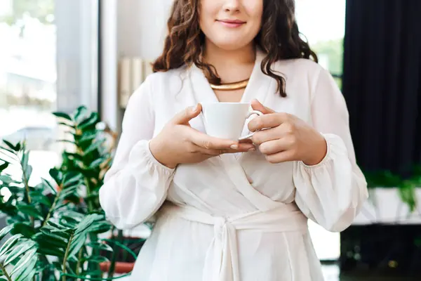 A young, beautiful plus size woman enjoys a warm cup of coffee in a cozy office setting. — Stock Photo