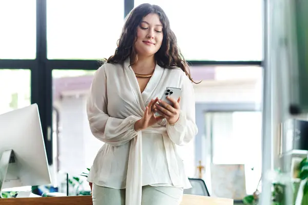 Uma mulher jovem, bonita e de tamanho grande está no escritório, sorrindo enquanto ela verifica seu telefone casualmente. — Fotografia de Stock