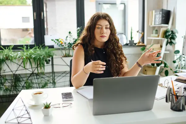 A confident plus size woman with long curly hair is actively engaging in work at a bright office, surrounded by plants. — Stock Photo