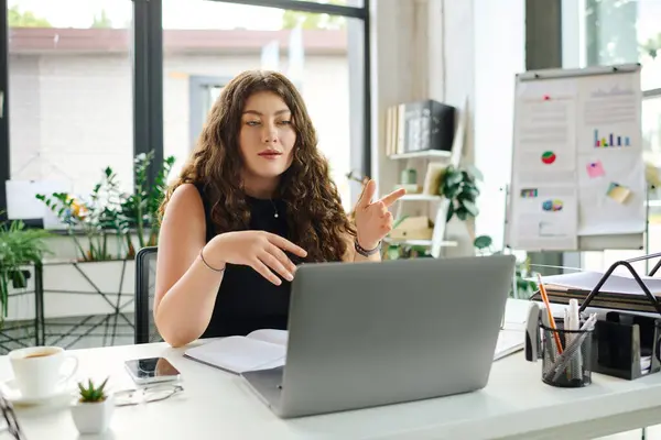 A confident young professional with curly hair is actively participating in a meeting while working at her desk. — Stock Photo