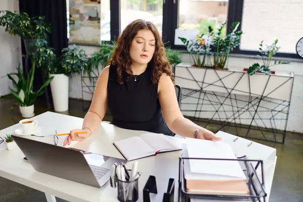 A young and beautiful plus size woman with curly hair focuses on paperwork in her stylish office, embodying corporate professionalism. — Stock Photo