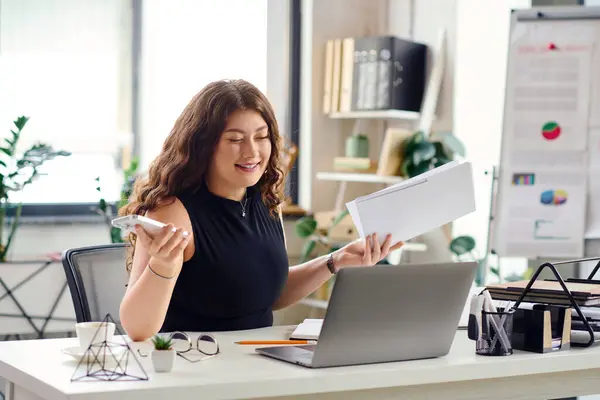 A confident plus size woman with curly hair interacts with documents while working at her desk in a bright office. — Stock Photo