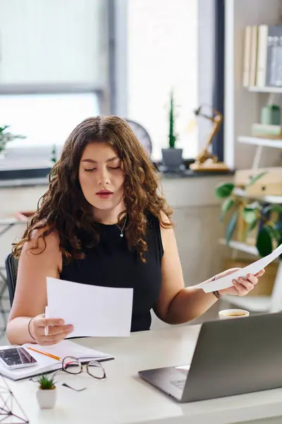 Una giovane donna sicura di sé con lunghi capelli ricci si impegna con i documenti di lavoro in un ambiente elegante ufficio, dimostrando professionalità. — Foto stock