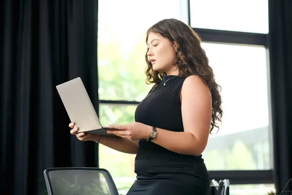 A confident plus size woman with long, curly hair works diligently on her laptop in a stylish office environment. — Stock Photo