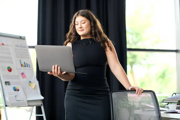 A confident plus size woman with long curly hair collaborates actively with her laptop in a stylish office setting. — Stock Photo