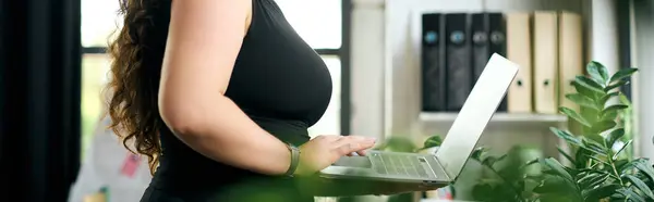 A dedicated young woman engages with her laptop in a vibrant office, showcasing corporate culture. — Stock Photo