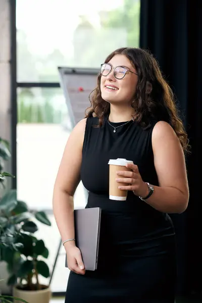 A joyful young woman with curly hair holds coffee and a notebook, exuding confidence in a contemporary office setting. — Stock Photo