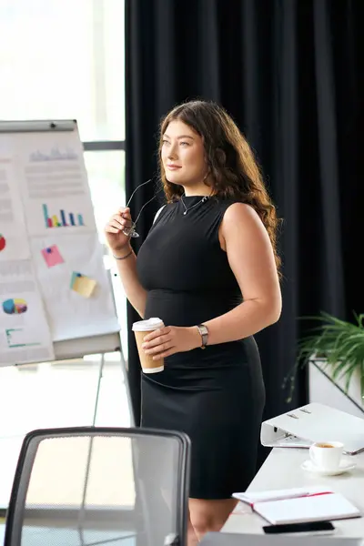 A young plus size woman with long curls stands in a modern office, holding a coffee and contemplating her next ideas during a meeting. — Stock Photo