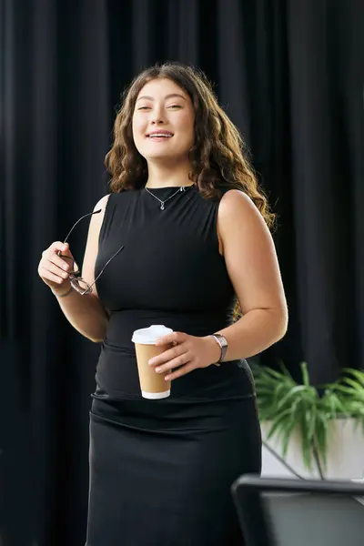 A plus-size professional with curly hair enjoys a coffee break while networking in a vibrant office environment. — Stock Photo