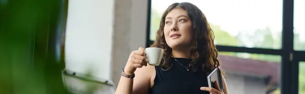 A vibrant plus size woman with long curly hair sips her coffee, deeply engaged in creative work at her modern office desk. — Stock Photo