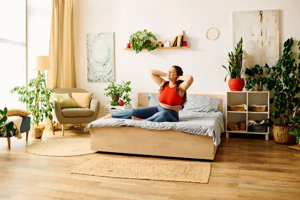 La jeune femme profite de son temps dans une chambre douillette, remplie de plantes, rayonnant de bonheur comme elle se détend sur son lit. — Photo de stock