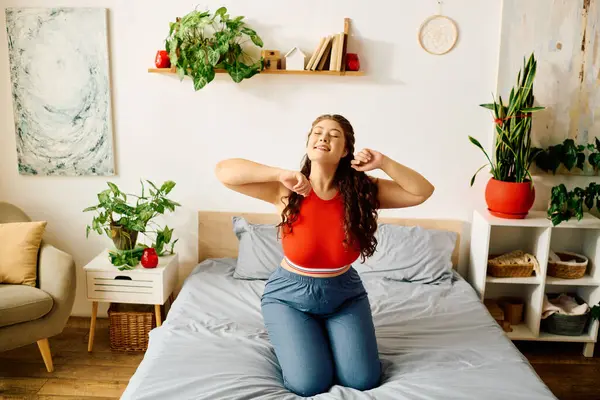 A young plus size woman smiles as she stretches playfully on her bed, surrounded by lovely plants and sunshine. — Stock Photo
