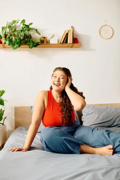 A young plus size woman with beautiful curly hair relaxes on her bed, radiating joy and warmth in her cozy home space. — Stock Photo