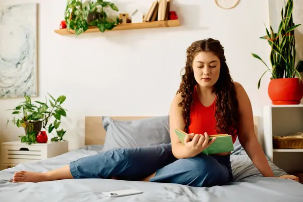 Una bella donna plus size si rilassa nella sua accogliente camera da letto, immersa in un libro mentre abbraccia un momento di calma. — Foto stock