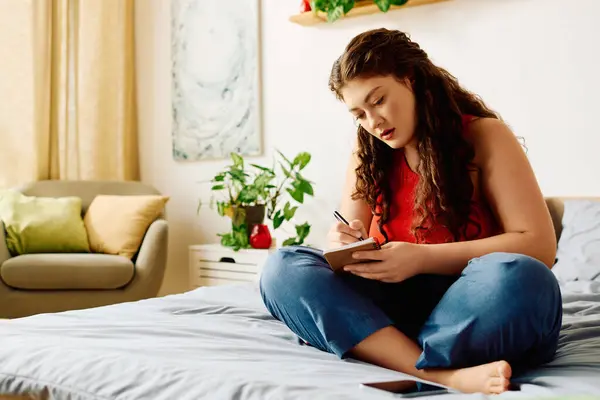 Curled up on her bed, a young plus size woman captures her thoughts in a journal, surrounded by a warm and inviting atmosphere. — Stock Photo