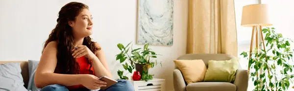 A young plus size woman with curly hair relaxes at home, holding her phone and soaking in the cozy atmosphere with greenery. — Stock Photo