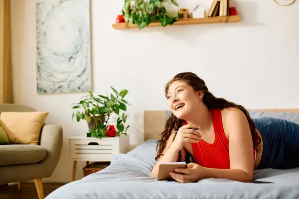 Веселая женщина plus size лежит на кровати, читает книгу и наслаждается своим временем в теплом и уютном пространстве. — стоковое фото