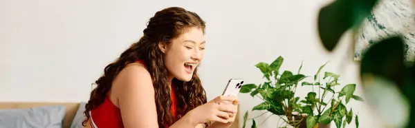 Una gioiosa donna plus-size con i capelli ricci sorride mentre interagisce con il suo telefono in un ambiente confortevole casa. — Foto stock