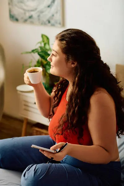 Una giovane donna plus-size con i capelli ricci assapora il suo caffè mentre annota i pensieri in un ambiente domestico sereno. — Foto stock