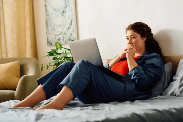 Uma jovem mulher plus size com cabelo encaracolado relaxa em casa enquanto se envolve com seu laptop, criando um ambiente acolhedor. — Stock Photo