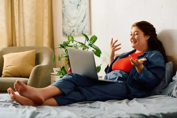A beautiful young woman with curly hair relaxes at home, engaging in a lively conversation while comfortably lounging on her bed. — Stock Photo