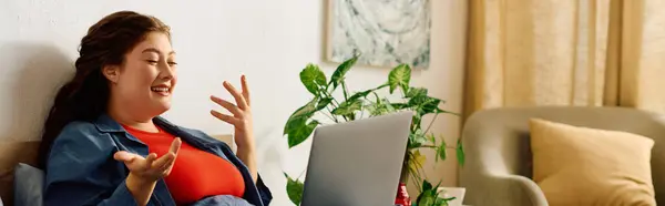 A cheerful young woman with curly hair engages in a lively conversation at home, surrounded by plants and comfort. — Stock Photo