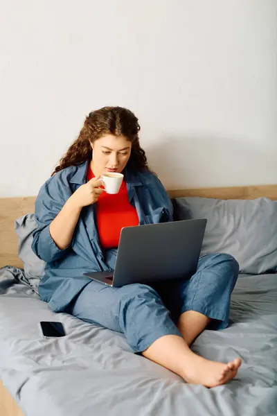 A young woman with beautiful curls savors her coffee as she engages on her laptop, embracing a cozy home atmosphere. — Stock Photo