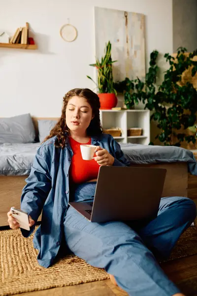Relaxing in her stylish home, a young plus size woman savors tea while exploring on her laptop. — Stock Photo