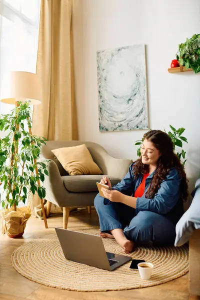A young woman with curly hair sits on the floor at home, radiating joy and comfort. — Stock Photo