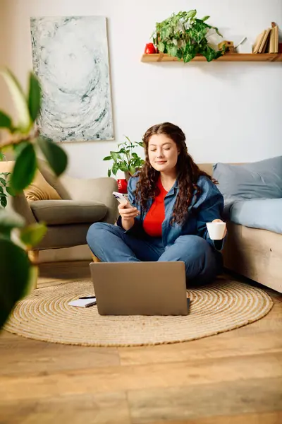 A cheerful young woman relaxes at home, engaging with her laptop while sipping a warm drink, surrounded by greenery. — Stock Photo