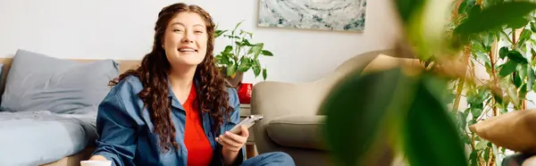 A cheerful young woman relaxes at home surrounded by plants while enjoying a moment of leisure with her phone. — Stock Photo