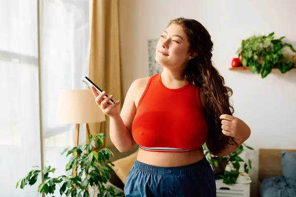 A young plus size woman with beautiful curly hair relaxes at home, holding her phone and smiling comfortably. — Stock Photo
